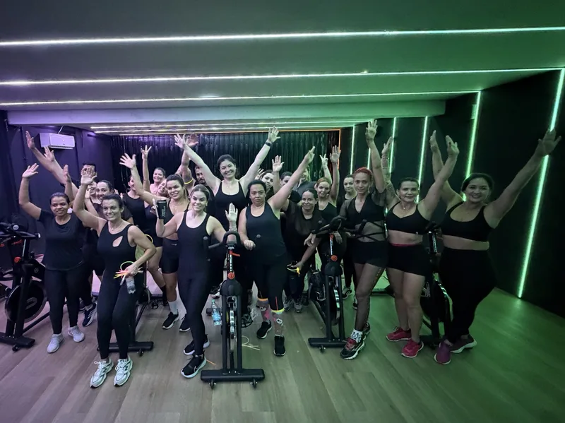 Karlla e a turma de Bike Indoor celebrando juntas, com os braços levantados no estúdio.